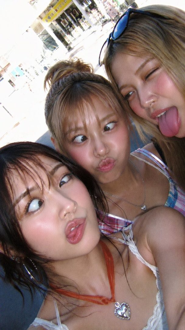 Three young East Asian women making funny faces for a selfie outdoors.