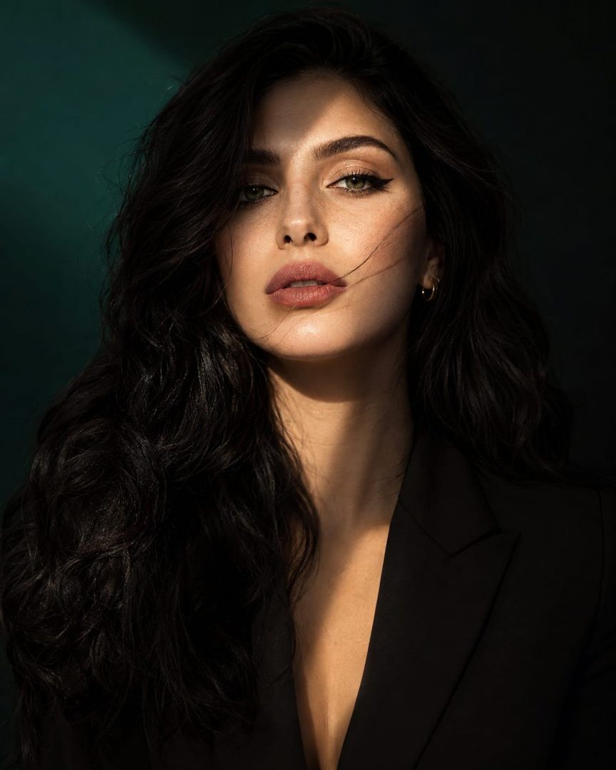 A striking portrait of a woman with long, dark wavy hair and emerald green eyes, illuminated by dramatic cinematic lighting.