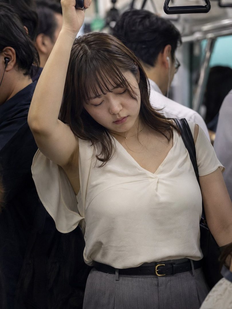 A young Japanese woman with her eyes closed, holding onto a pole on a crowded train.