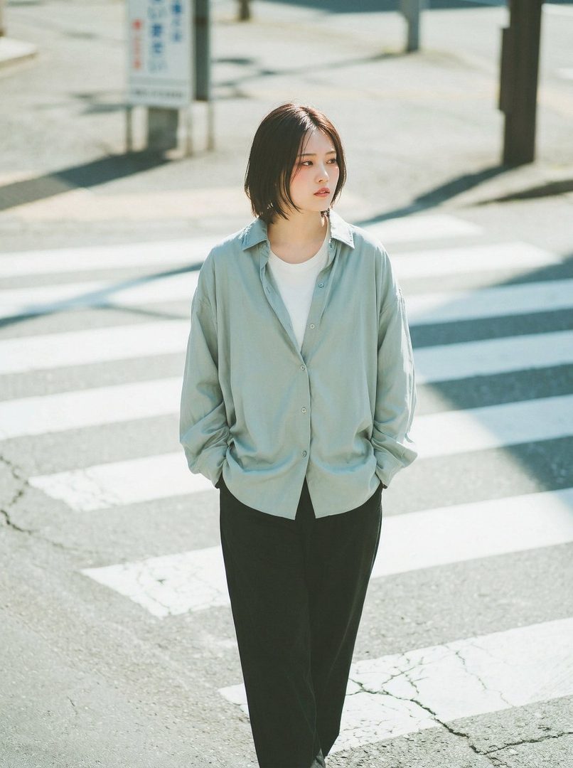 A young woman with short black hair stands on a crosswalk, looking to the side.