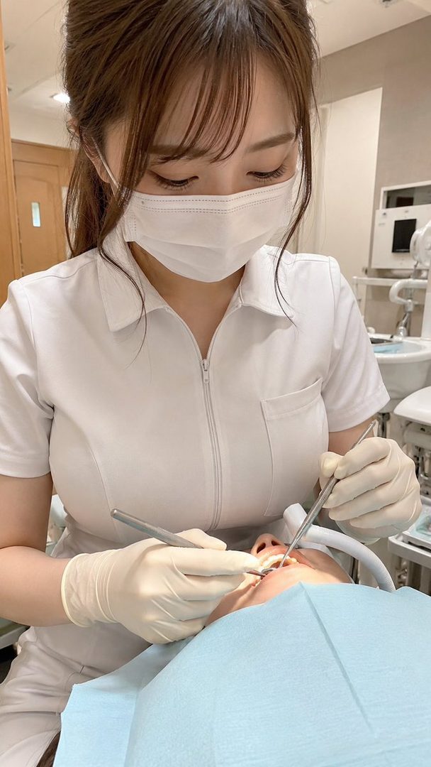 A female dentist wearing a white uniform and mask, performing a dental examination on a patient.