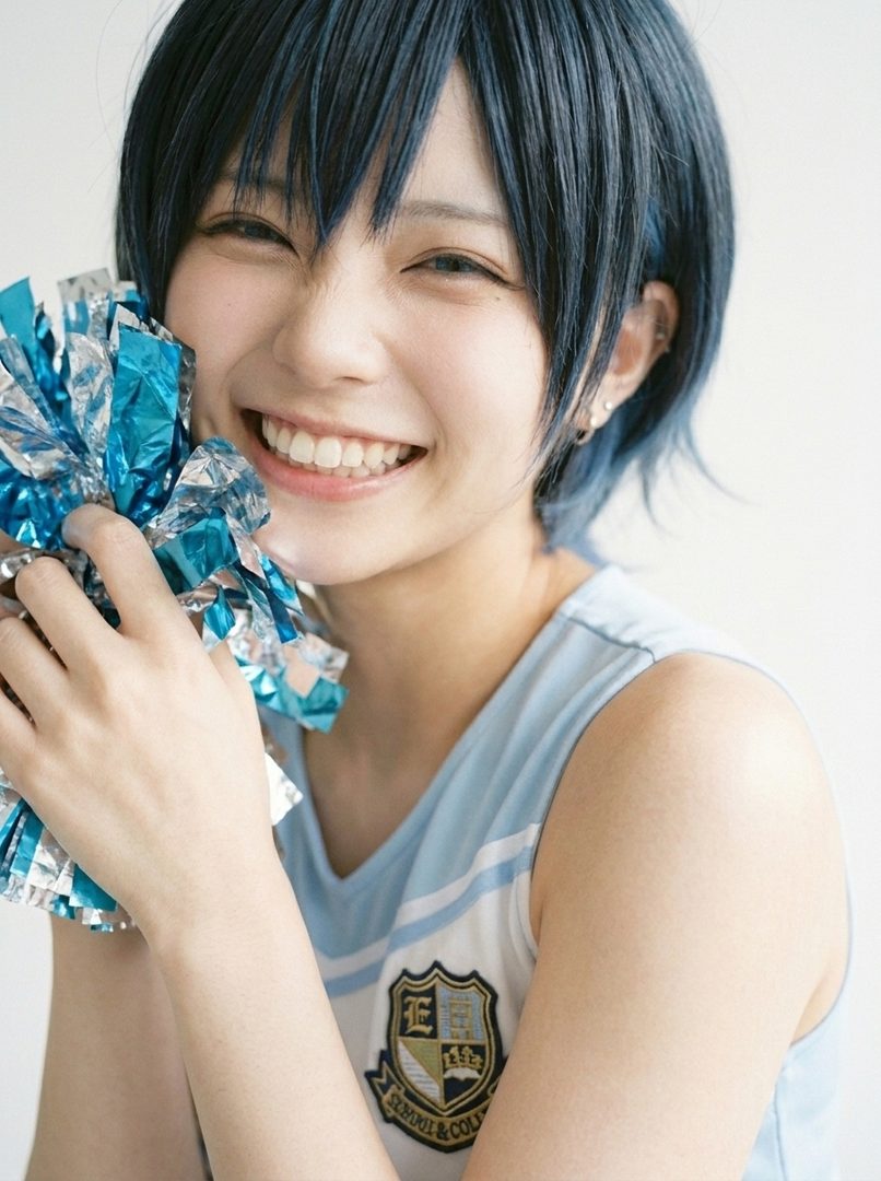 A young woman with short blue hair smiles brightly, holding a blue and silver pom-pom.
