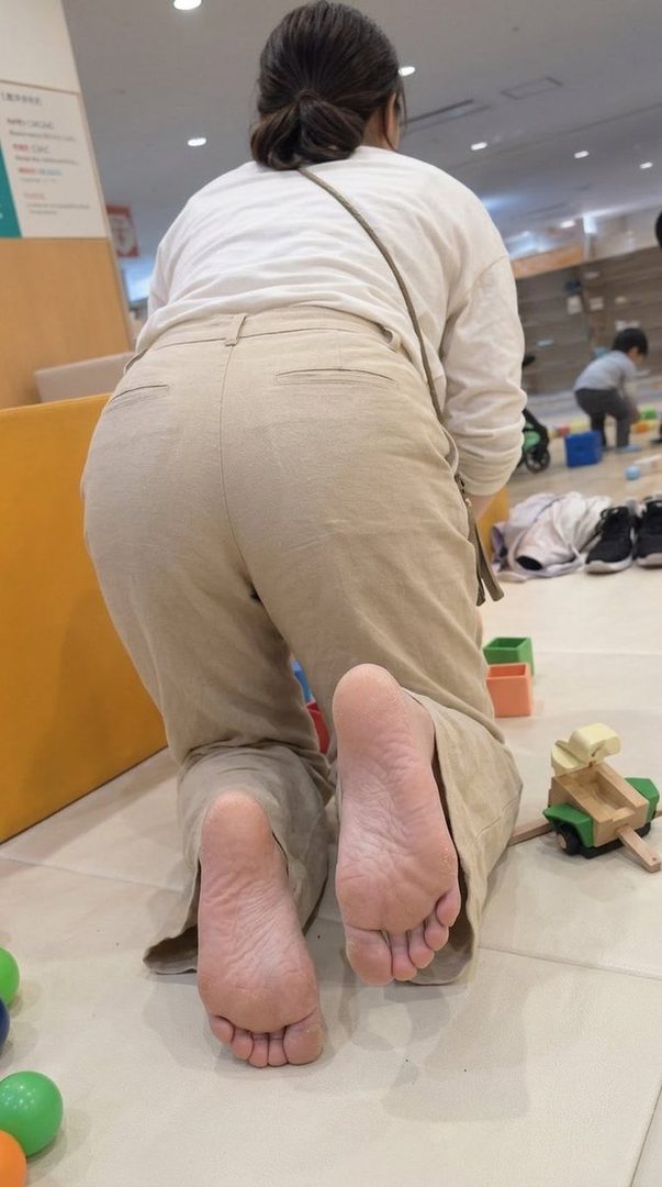 A person in casual clothes is kneeling on the floor, showing the soles of their feet, in an indoor setting with toys nearby.