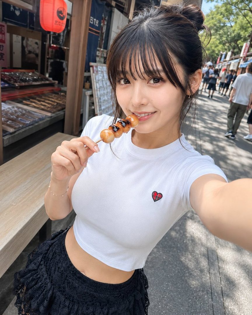A young Japanese woman with her hair in a bun, wearing a white crop top and black lace skirt, smiles at the camera while holding a skewer of dango (sweet dumplings). She is standing on a street with shops and people in the background.