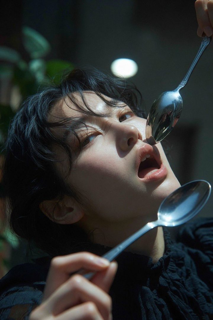 A close-up portrait of an AI-generated woman with black hair, playfully holding two spoons near her mouth.