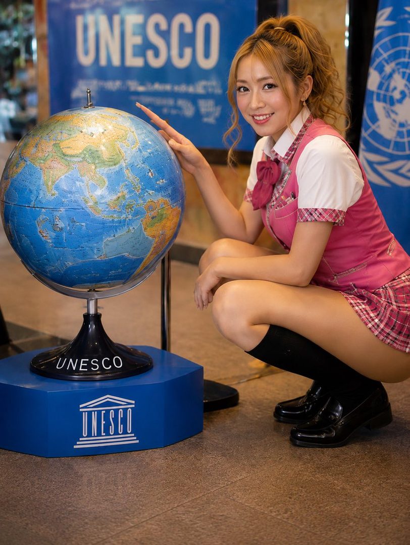 A young woman in a pink school uniform poses next to a globe with the UNESCO logo.