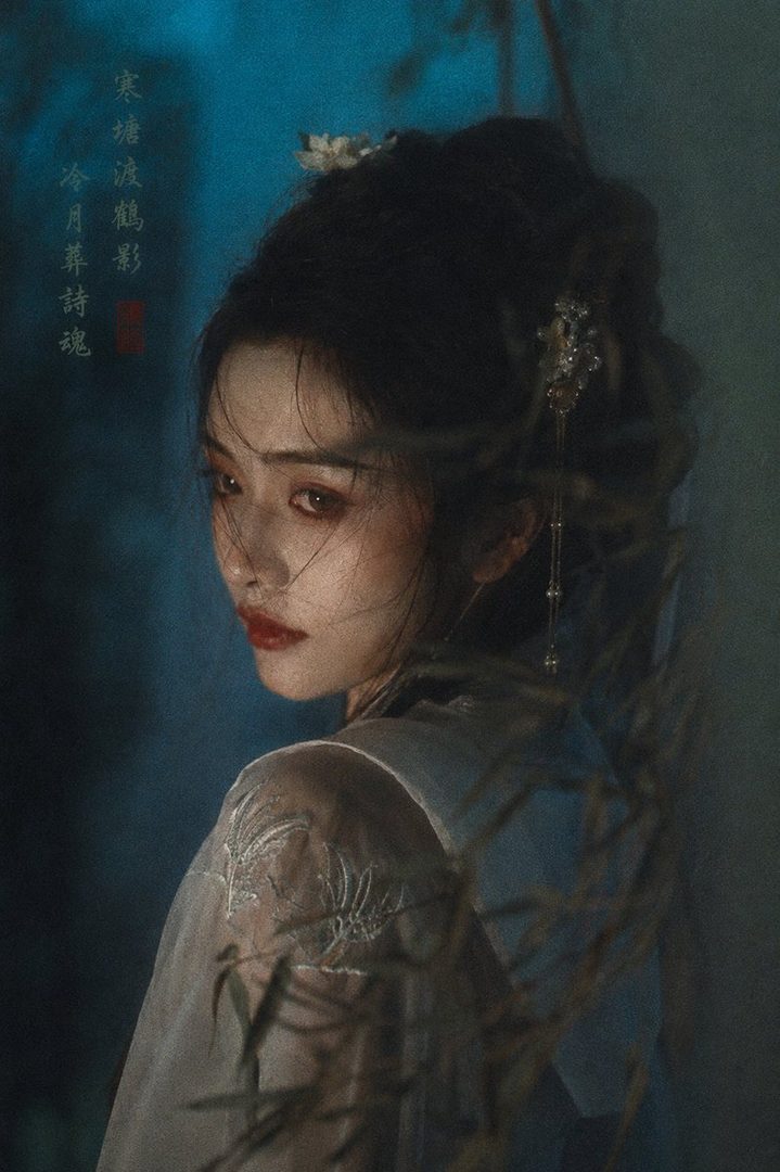A beautiful East Asian woman with dark hair styled up, wearing traditional clothing, looks over her shoulder with dramatic makeup in a dimly lit, atmospheric outdoor setting.
