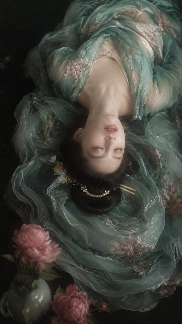 A photorealistic portrait of a woman in a flowing, ethereal gown with floral embroidery, lying down with her eyes closed.