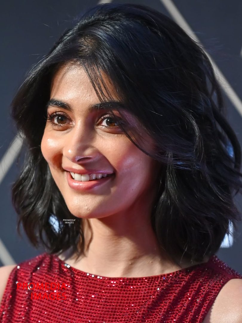 A close-up portrait of a woman with short black hair and a red sequined dress, smiling warmly.