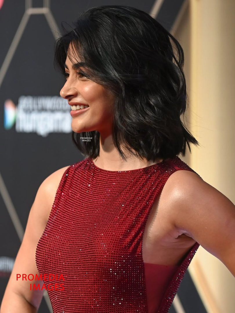 A woman with short black hair and a red sequined dress smiles, captured in a profile shot.