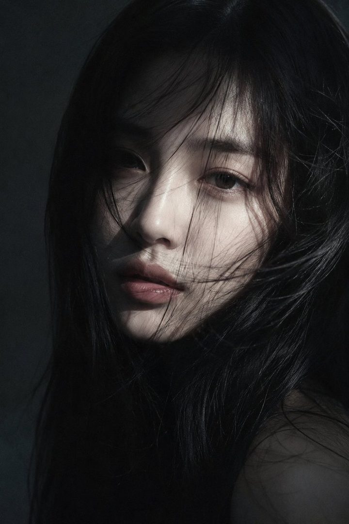 Cinematic close-up portrait of a young East Asian woman with long, dark, slightly messy hair blowing across her face, soft pink lips, and expressive eyes, set against a dark, moody background with dramatic low-key lighting.