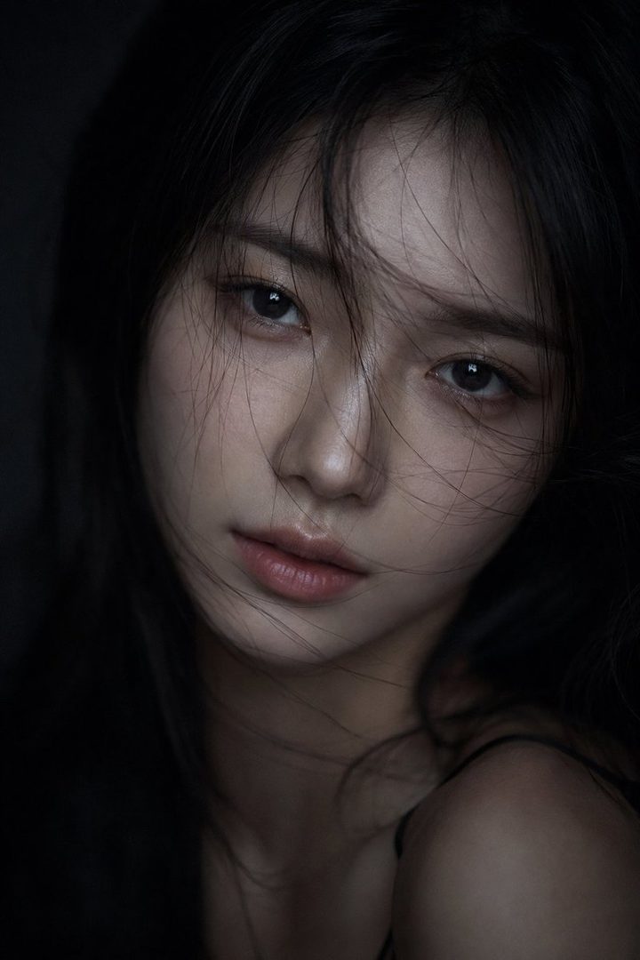 Close-up cinematic portrait of an East Asian woman with long, slightly messy black hair, porcelain skin, and expressive eyes, set against a dark, moody background with dramatic low-key lighting.