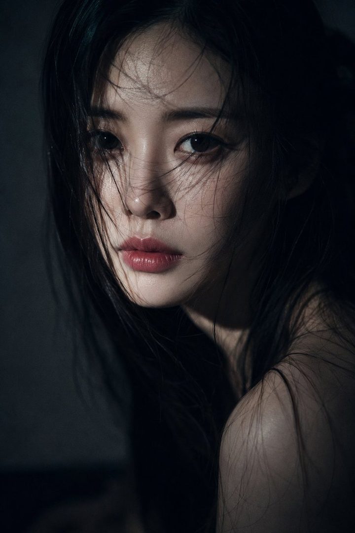 Close-up cinematic portrait of a young East Asian woman with long, dark, slightly messy hair falling across her face, porcelain skin, and deep expressive eyes, looking calmly and melancholically into the camera.