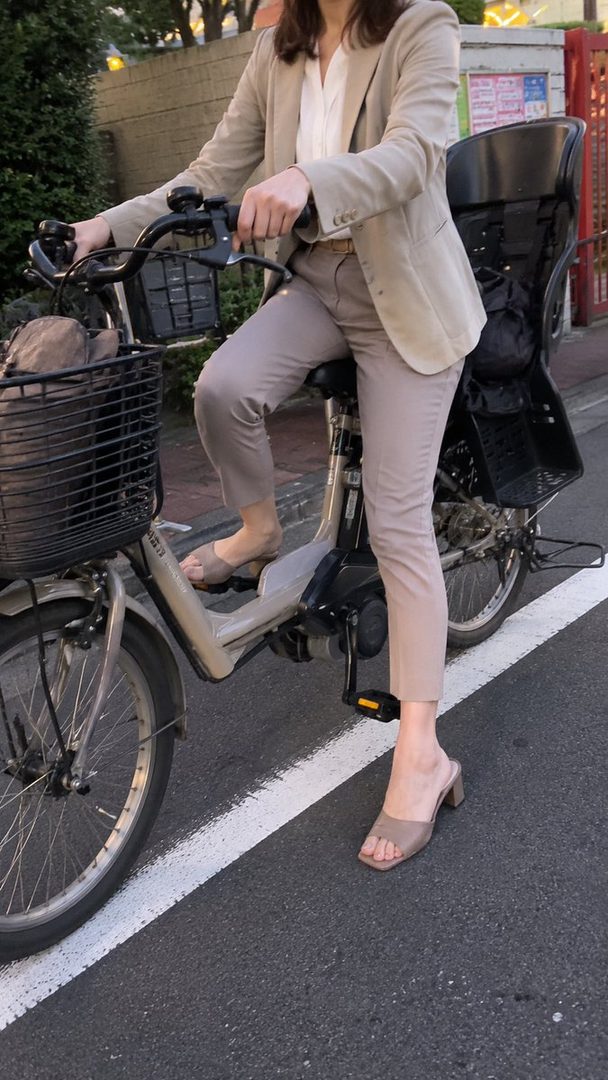 A woman in a beige blazer and light pants is riding a bicycle on a street.