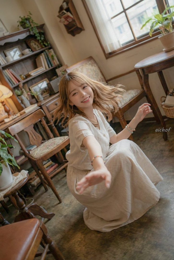 A young woman with blonde hair smiles and poses indoors in a casual outfit.