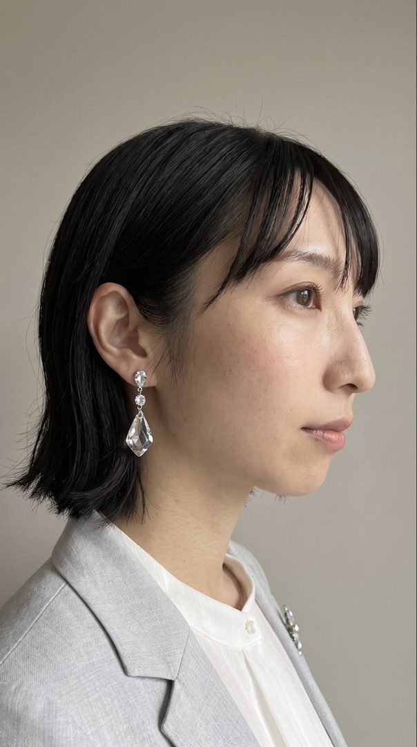 Profile portrait of an East Asian woman with short black hair, wearing a light grey blazer over a white blouse and large crystal earrings.
