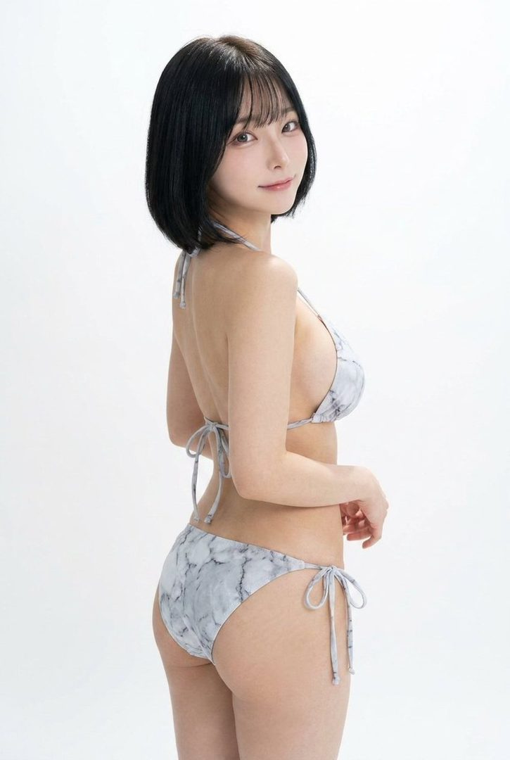 A young woman with short black hair and bangs, wearing a marble-patterned bikini, poses in a studio setting.