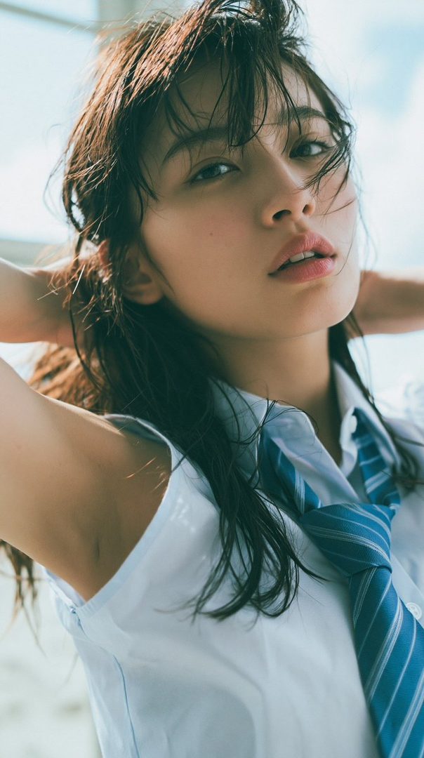 A young woman with wet brown hair, wearing a white blouse and blue striped tie, poses with her hands behind her head.