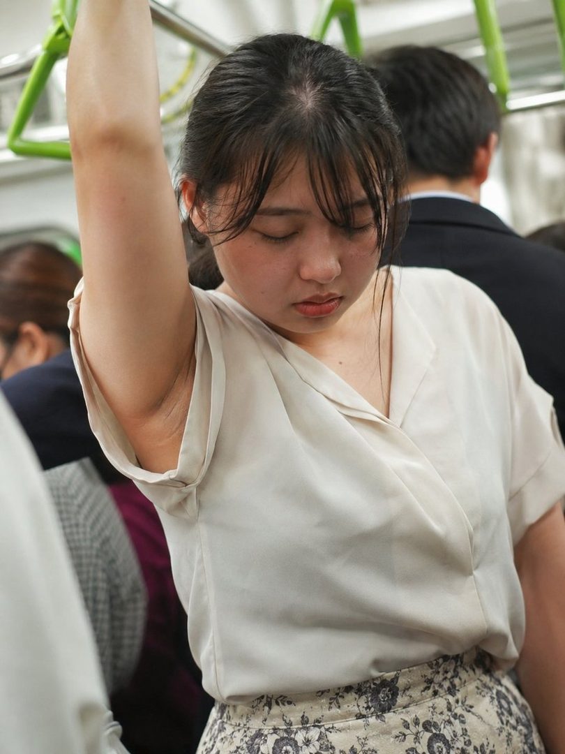 A young East Asian woman with her eyes closed, holding onto a train handrail.