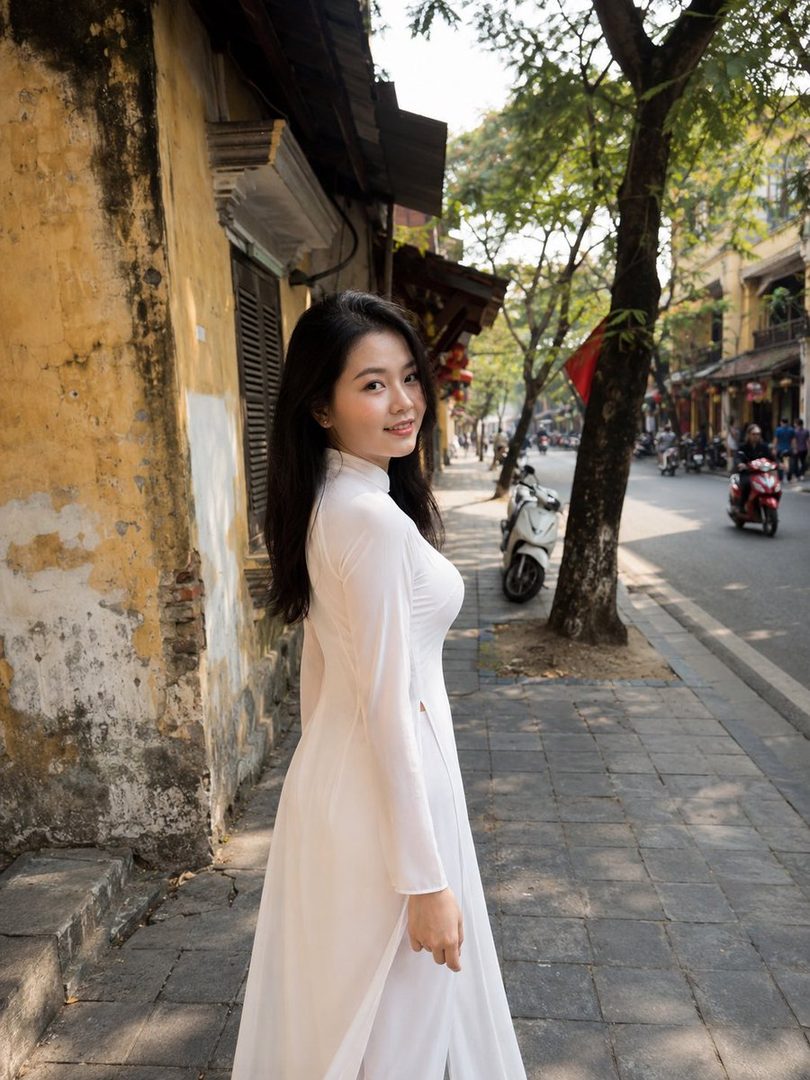 A young woman in a white traditional Vietnamese dress walks down a street in Vietnam.
